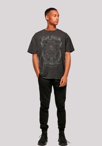 Black oversized T-shirt with a graphic print featuring skull and wings, made of cotton. Paired with black sweatpants and black sneakers.