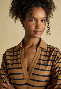 Lühikeste varrukate ja pruunide triipudega polo-särk, millel on tumesinised triibud, kaelusstiilis kaelus ja väike logo rinnal. Sile kangas.