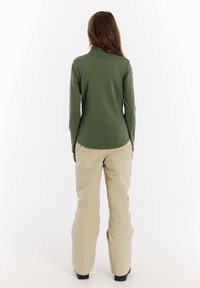 Groen langemouwtop met een hoge kraag, gecombineerd met lichtbeige loszittende broek. Soepele stof, ontworpen voor comfort en bewegingsvrijheid.