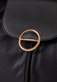 Black leather bag flap with textured fabric and round gold clasp engraved with "Borbonese" securing closure.
