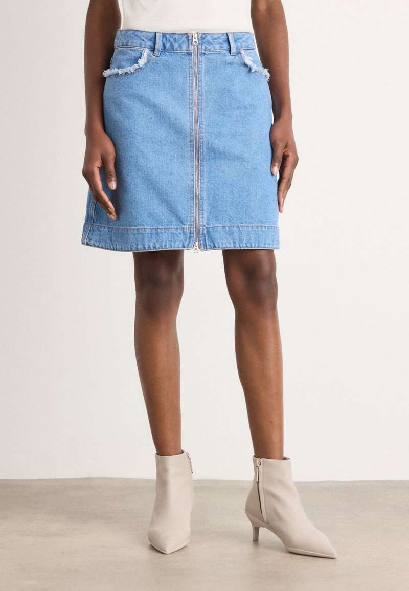 Denimskjørt med glidelås foran, frynsete lommekanter, lyseblå vask, kne-lengde, kombinert med beige ankelstøvler. Glatt tekstur.