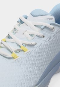 Baskets Skechers bleu clair avec lacets blancs, serrures de lacets jaunes et dessus en tissu texturé en gros plan.
