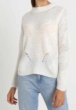 Maglione bianco lavorato a maglia con taglio morbido, caratterizzato da un collo a costine e un motivo traforato, abbinato a jeans in denim blu chiaro.