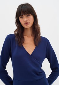 Navy blue wrap top with long sleeves and a deep V-neck. Made from smooth, stretchy fabric with a fitted silhouette.