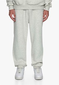 Gray, soft, cotton sweatpants with an elastic waistband and cuffs. Paired with white sneakers, featuring textured soles and lacing.