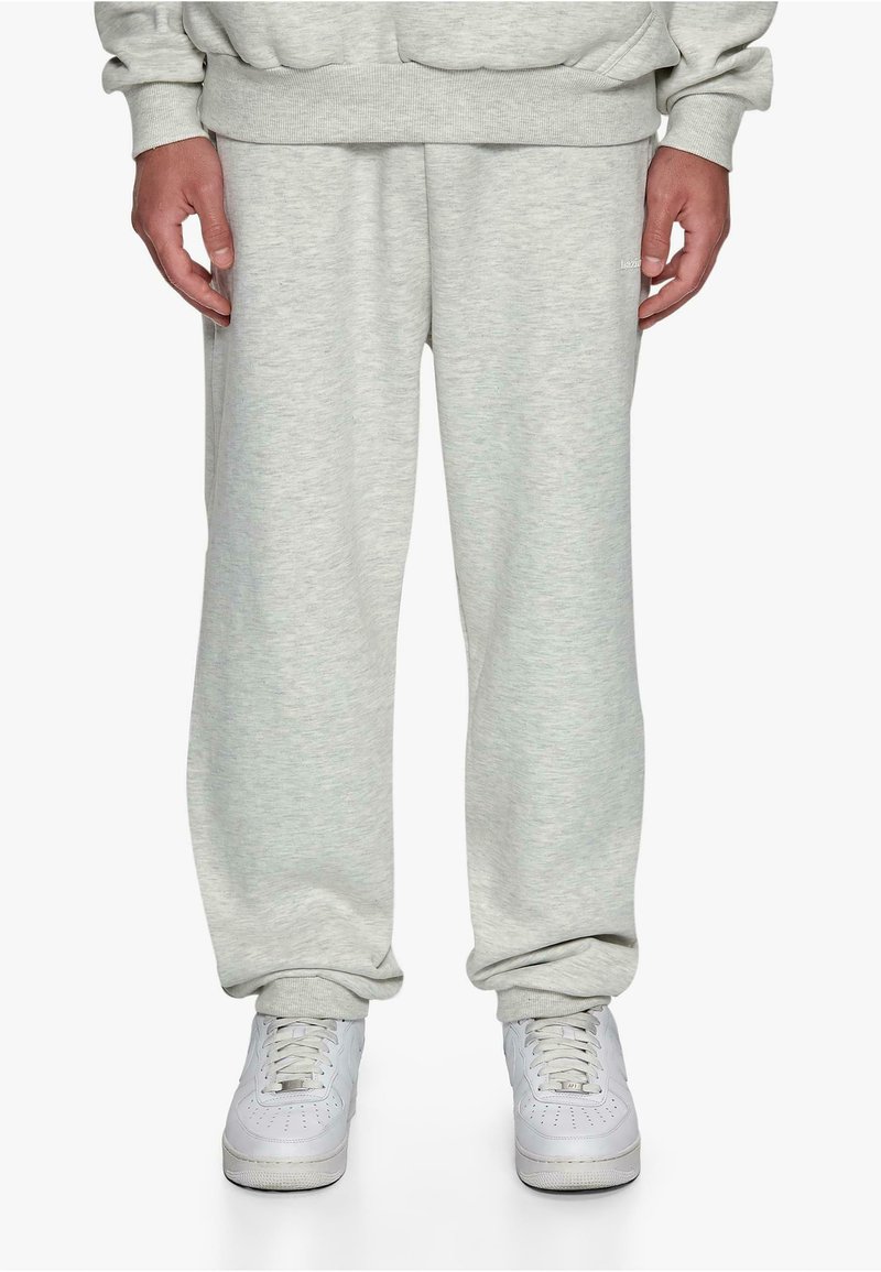 Gray, soft, cotton sweatpants with an elastic waistband and cuffs. Paired with white sneakers, featuring textured soles and lacing.