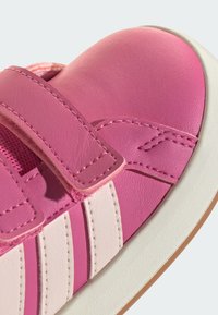 Ružičasta kožna cipela s čičak trakom, sadrži svijetloružičaste pruge, zaobljeni vrh i teksturiranu gornju površinu. Gumeni potplat s glatkim završetkom.