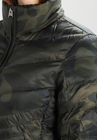 Doudoune en motif camouflage vert foncé, avec un col montant et des coutures verticales. Le matériau semble brillant et lisse.