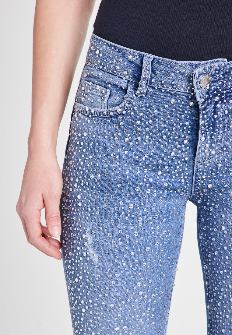 Jeans in denim blu con un design strappato e decorazioni in strass sparse, stile a cinque tasche e una forma aderente.