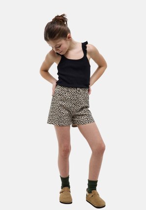 Jeune fille regardant vers le bas, portant un débardeur noir à bretelles à volants, un short à motifs léopard, des chaussettes vertes et des chaussures beige à enfiler.