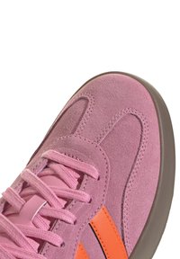 Närbild av rosa mockaskor med matchande snörning, orange sidlist och ljusbrun sula.