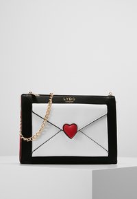 Borsa a forma di busta in bianco e nero con un accento a forma di cuore rosso, tracolla in catena dorata e dettaglio del logo. Texture liscia con colori contrastanti.