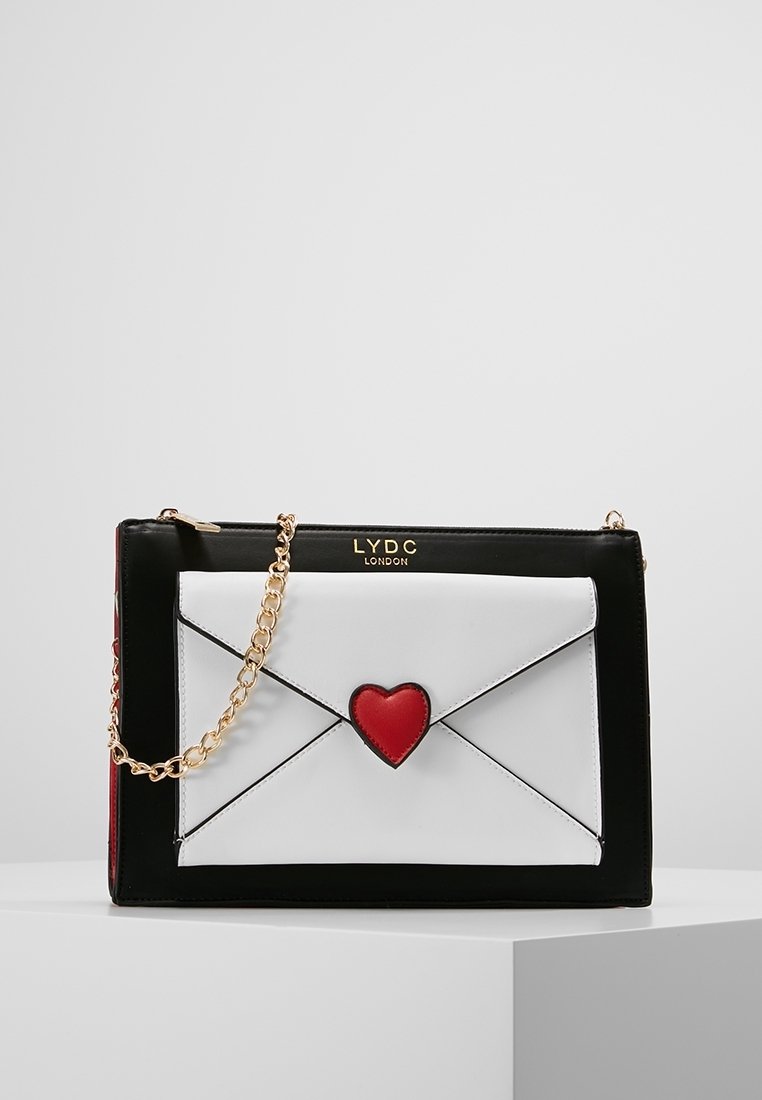 Borsa a forma di busta in bianco e nero con un accento a forma di cuore rosso, tracolla in catena dorata e dettaglio del logo. Texture liscia con colori contrastanti.