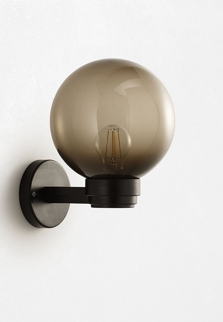 Zwarte wandlamp met een ronde, rokerige glazen bol. Bevat een blootgestelde gloeilamp, solide metalen basis en een horizontale arm.