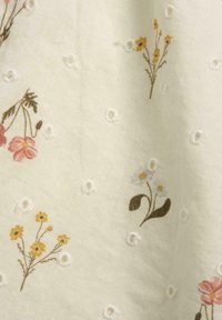 Tissu brodé floral avec un fond crème. Présente des fleurs roses, jaunes et bleues, avec de petits détails en œillets répartis.