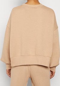 Světle béžová oversized mikina s vroubkovaným kulatým výstřihem a manžetami, s hladkou texturou a lehce spuštěnými ramenními švy.