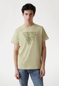 Šviesiai žalia medvilninė marškinėliai trumpomis rankovėmis su dideliu reljefiniu trikampio logotipo dizainu centre.