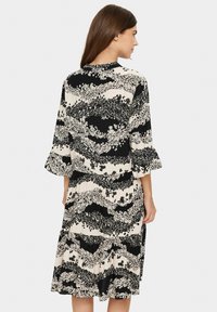 Kukallinen mekko, jossa on liehukkeet ja mustavalkoinen värimaailma. Kevyt kangas, polven pituinen muotoilu, jossa on kerroksellinen helma.