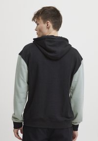 Felpa con cappuccio caratterizzata da un corpo nero e maniche verde chiaro, realizzata in tessuto morbido. Ha una tasca a marsupio e polsini a costine.