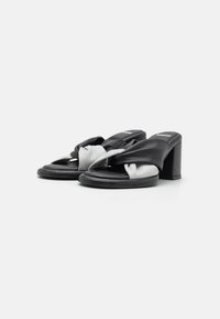 Black and white twisted leather open-toe heeled sandals with block heels on a plain white background.