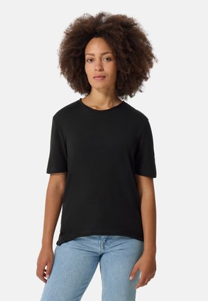 Schwarzes Baumwoll-T-Shirt mit rundem Halsausschnitt und kurzen Ärmeln, das einen lässigen Schnitt und einen leicht abgerundeten Saum hat. Getragen mit hellblauen Jeans.