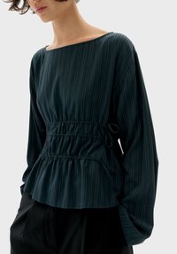 Blusa verde scuro realizzata in tessuto leggero, con righe verticali, scollatura quadrata e vita elasticizzata con dettagli a laccio.