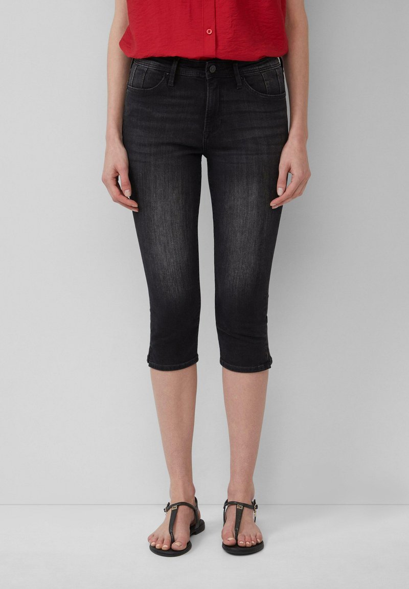 Krótkie czarne dżinsowe capri do kolan z dopasowanym krojem, pięcioma kieszeniami i podwiniętymi nogawkami. Połączone z brązowymi płaskimi sandałami i czerwoną koszulą.