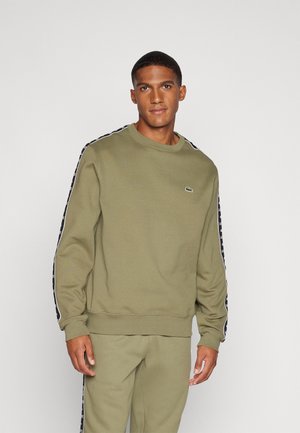 Sudadera verde oliva hecha de tela suave, con puños y dobladillo acanalados, que presenta franjas laterales negras con un patrón de logo.
