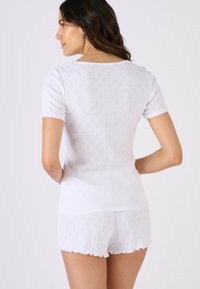 Conjunto de ropa de descanso blanca con mangas cortas, bordes con diseño festoneado y un patrón texturizado de diamantes. La parte superior se combina con unos shorts a juego.