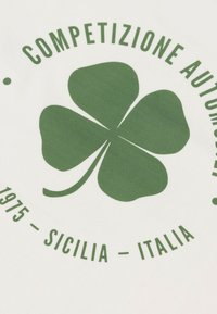 Tejido blanco con un gráfico de un trébol de cuatro hojas verde y el texto "Competizione Automobilistica 1975 - Sicilia - Italia" que lo rodea.