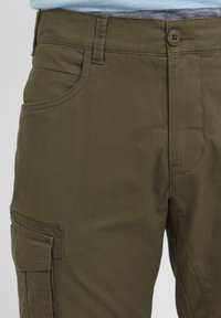 Pantalons cargo vert olive en mélange de coton durable, dotés de poches latérales, d'une fermeture à bouton et de détails de couture multiples.