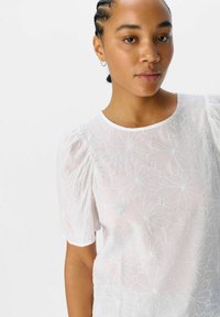 Witte blouse met korte pofmouwen, voorzien van een geborduurd bloemenpatroon en een ronde halslijn, gemaakt van lichtgewicht, doorschijnende stof.