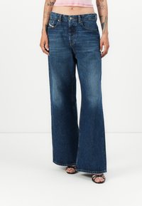 Jeans de ganga de perna larga em azul escuro, com um design clássico de cinco bolsos e um ligeiro desvanecimento na bainha, com costuras detalhadas e fecho de botão.