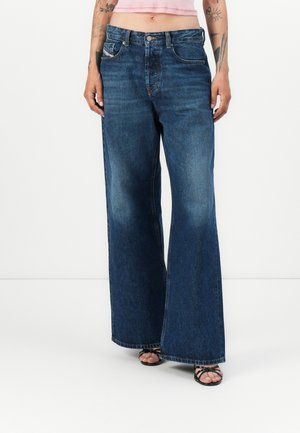 Bredde ben denim jeans i mørkeblå, med et klassisk fem-lomme-design og lett falming ved kanten, syddetaljer og knappelukking.