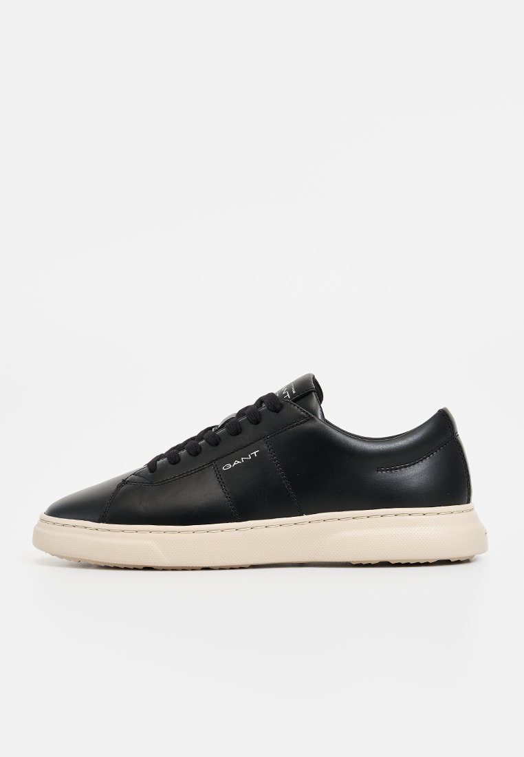 Sneaker in pelle nera con forma arrotondata, suola in gomma bianca e marchio discreto sul lato. Presenta chiusura con lacci e texture liscia.