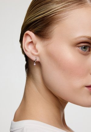 Srebrna kolczyk w kształcie obręczy z małym różowym kamieniem, pokazany na uchu modelki. Projekt jest elegancki i minimalistyczny.