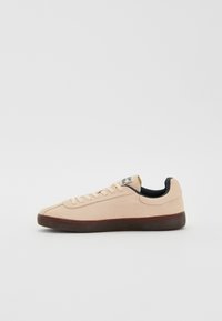 Zapatilla de ante rosa claro con forma plana, punta redonda, forro interior negro y suela de goma oscura. Incluye cordones y etiqueta en la lengüeta.