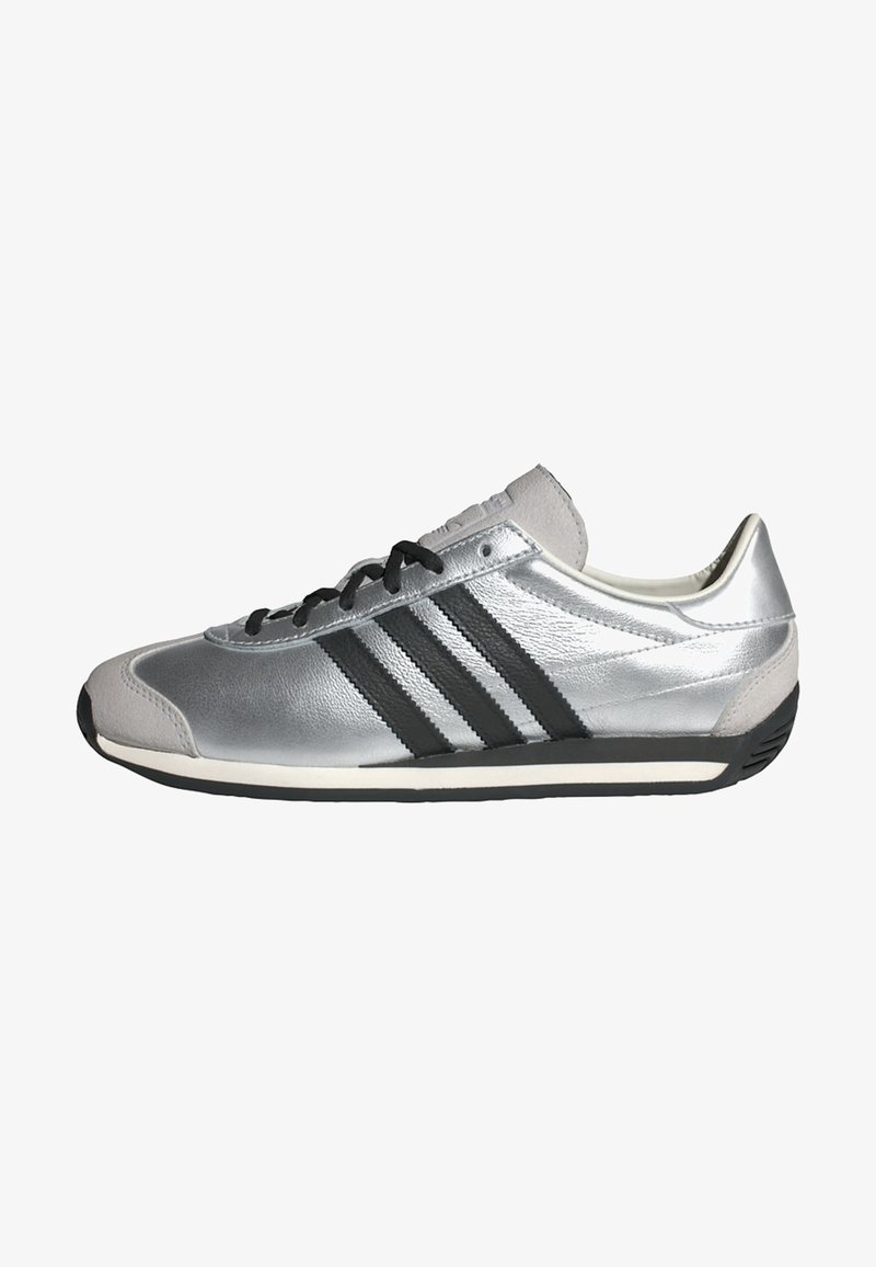 Srebrny but sportowy z gładką skórzaną powierzchnią, czarnym wzorem z trzema paskami oraz czarnymi sznurowadłami. Posiada zaokrąglony nosek i gumową podeszwę.