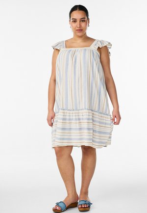 Femme portant une robe sans manches, longueur genoux, rayée verticalement bleu et beige avec des bretelles volantées, associée à des sandales bleues à bout ouvert.