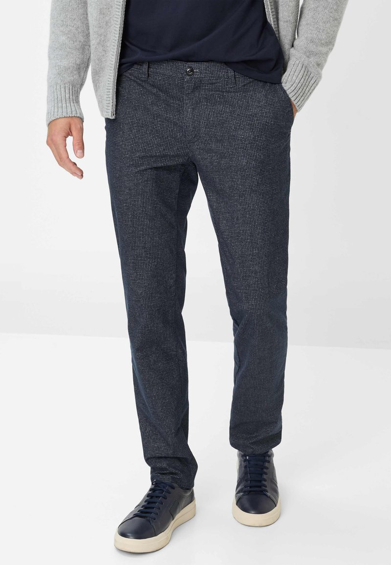 Navy-gepatroneerde broek van gestructureerde stof, met een knoopsluiting en zijzakken, gecombineerd met donkere sneakers.