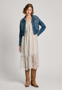Chaqueta de denim con un diseño ajustado, vestido maxi de estampado floral en colores claros y botas vaqueras de ante en tono marrón claro hasta la rodilla con detalles de costura.