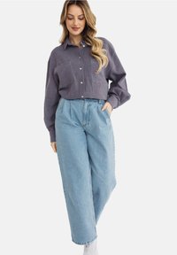 Szary koszula na guziki z dwoma kieszeniami na piersi, w połączeniu z jasnoniebieskimi spodniami o szerokich nogawkach. Gładkie tekstury z widocznym przeszyciem i luźny krój.