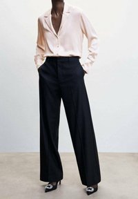 Blusa di raso rosa chiaro con maniche lunghe e colletto, abbinata a pantaloni neri a gamba larga e tacchi alti neri con dettagli gioiello.