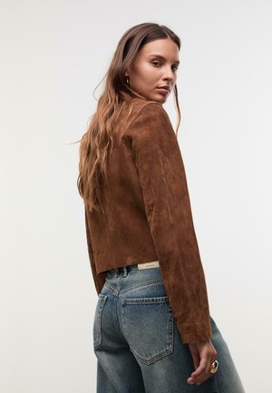 Braune Wildlederjacke mit einem cropped Design, mit langen Ärmeln und einer glatten Textur, kombiniert mit hochtaillierten blauen Jeans.