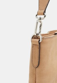 Beige læderhåndtaske med glat tekstur, der har en sølvfarvet lukning og et præget logo på remmen. Enkel design med rene linjer.