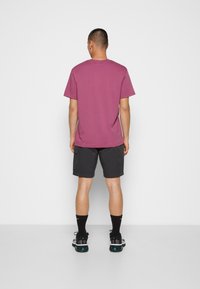 T-shirt med kort ärm och rund halsringning i mauve, matchad med mörkgrå shorts. Avslappnad fotbeklädnad med mönstrade detaljer och svarta strumpor.