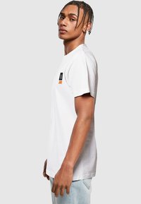 Tricou alb din bumbac, cu mâneci scurte, având un mic logo multicolor pe piept. Croială dreaptă și textură moale.