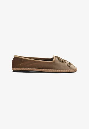 Chaussure plate marron avec des décorations en perles dorées sur l'avant et un bord de semelle en tissu, vue de côté sur fond blanc.