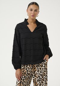 Blusa nera con texture e motivo ondulato, colletto e maniche lunghe. Abbinata a pantaloni con stampa leopardata.