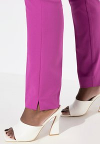 Pantaloni rosa aderenti con spacchi laterali, abbinati a mule bianche con apertura frontale e tacco quadrato dal finish lucido.